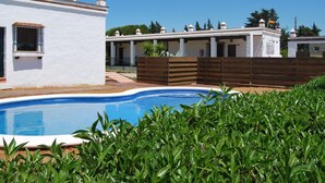 A pool area with a white building, wooden fence, and greenery.