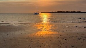 Una playa con un velero y huellas en la arena.