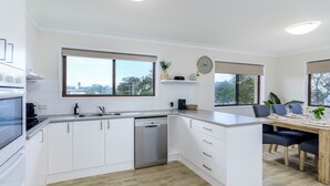Una cocina moderna con armarios blancos, lavavajillas y un comedor con mesa y sillas de madera.