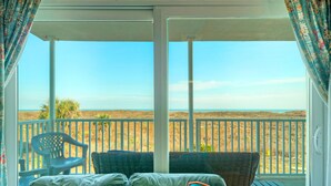 A balcony with a view of the beach, wicker furniture, and a plastic chair. - Beachfront Condo w/ Ocean View, 2 Pools, Boardwalk to the Beach | Island Getaway (Port Aransas)
