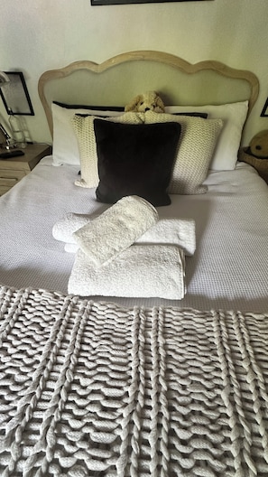 A neatly made bed with a textured blanket, a black pillow, and a stuffed animal.