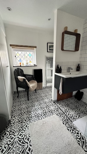 A bathroom with a black and white patterned floor, a black chair, a white sink, and a mirror above the sink.