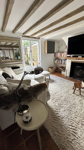 A cozy living room with a white sofa, a small round table, a bookshelf, a fireplace, and a large window.