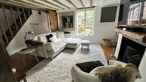 A cozy living room with a white sofa, a small ottoman, a fireplace, and a staircase leading to another level.