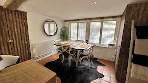 A dining area with a wooden table, chairs, a black furry rug, a mirror, and a window with blinds.