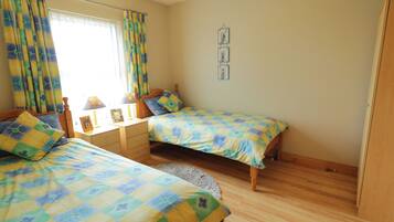 A bedroom with two single beds, a wooden dresser, a nightstand, a lamp, and a window with curtains.