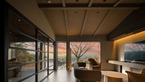A modern interior with a large window offering a scenic view, a dining area with a round table and chairs, and a flat-screen TV mounted on the wall. - Kirinosato (Kirishima)