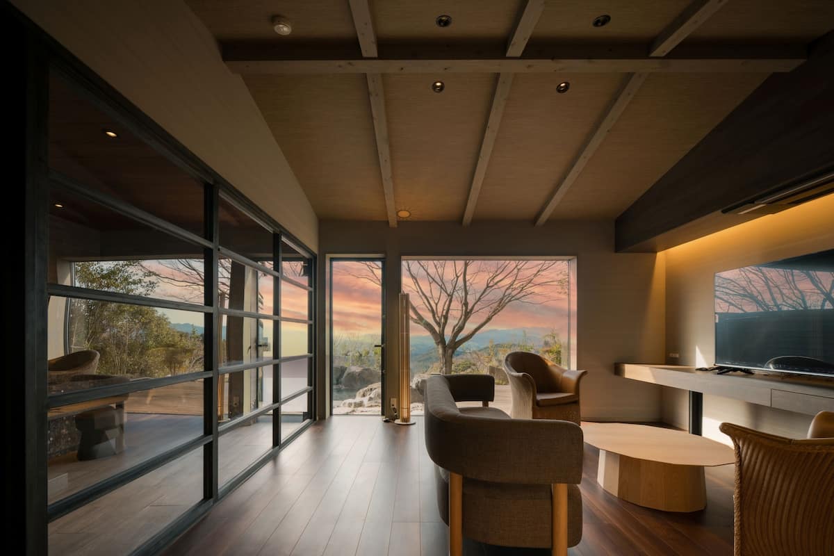 A modern interior with a large window offering a scenic view, a dining area with a round table and chairs, and a flat-screen TV mounted on the wall.
