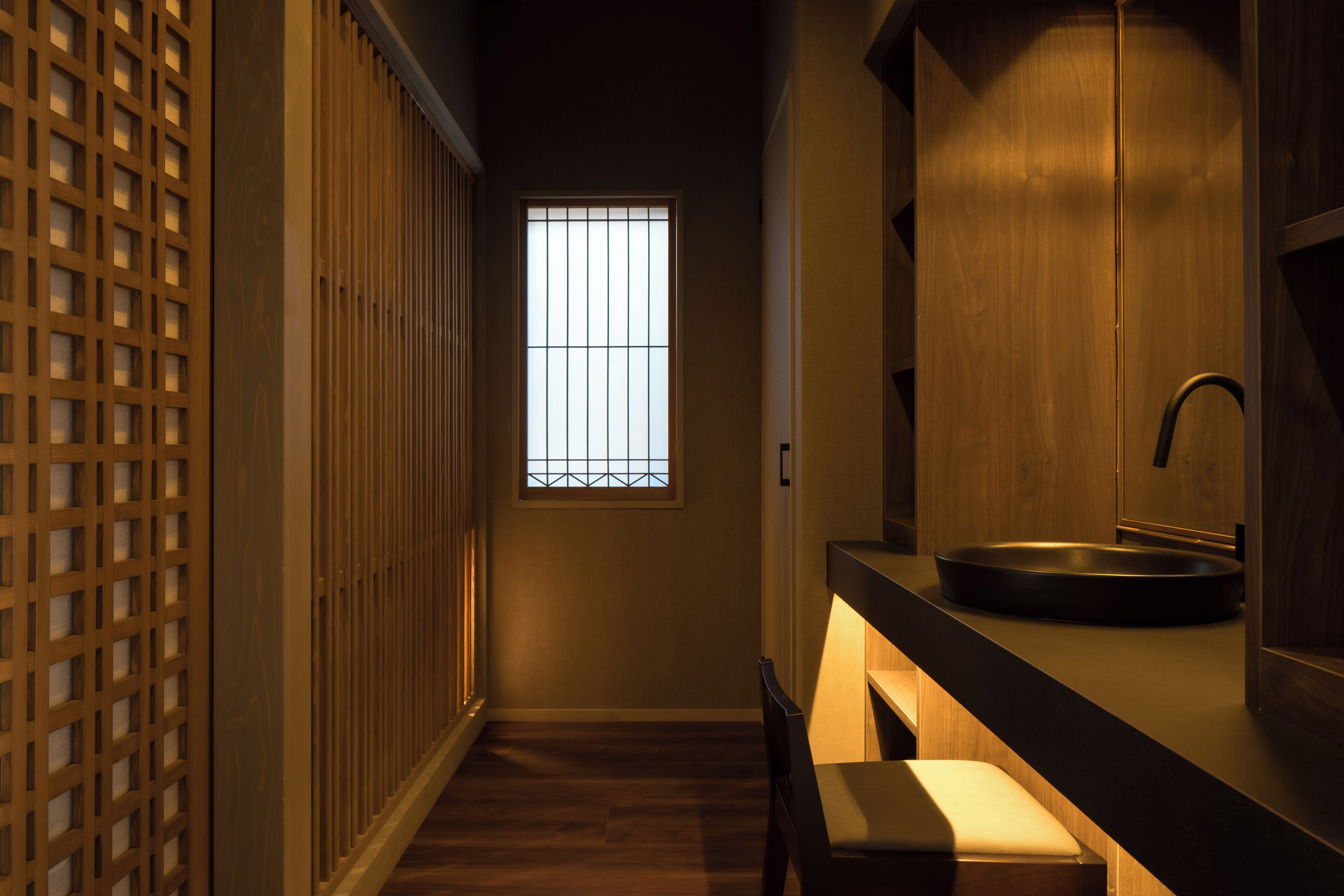 Un pasillo estrecho con suelo de madera, una ventana con barrotes verticales y un lavamanos con espejo.