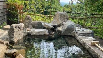 Un manantial termal con rocas grandes y una terraza de madera.