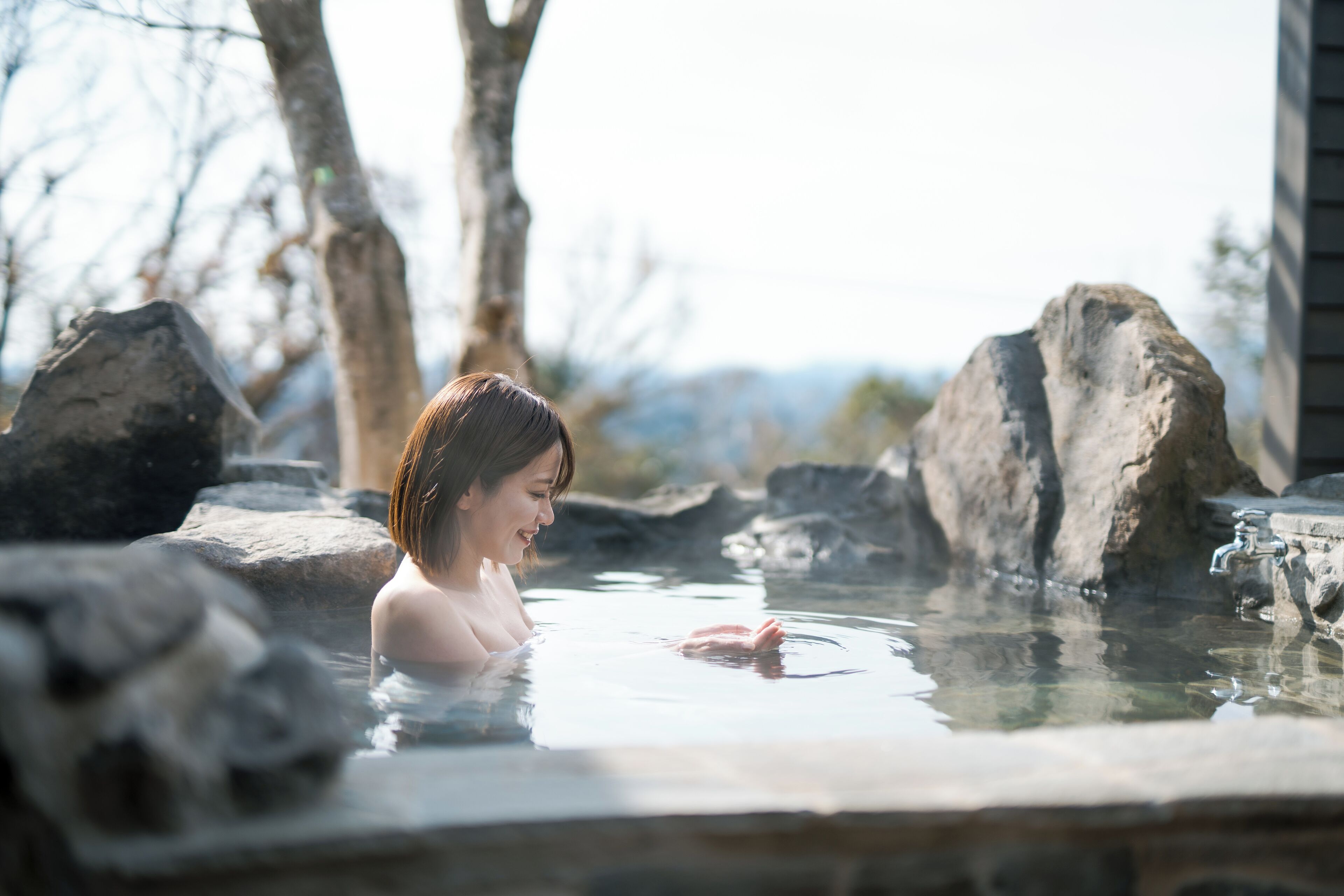 A person in a hot spring surrounded by large rocks and trees.