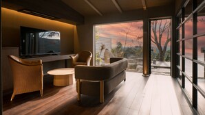 A modern living room with a flat-screen TV, wicker chairs, a round coffee table, and a large window offering a view of the outdoors. - Kirinosato (Kirishima)