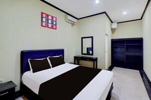 A hotel room with a bed, bedside table, mirror, wardrobe, and wall-mounted air conditioning unit.