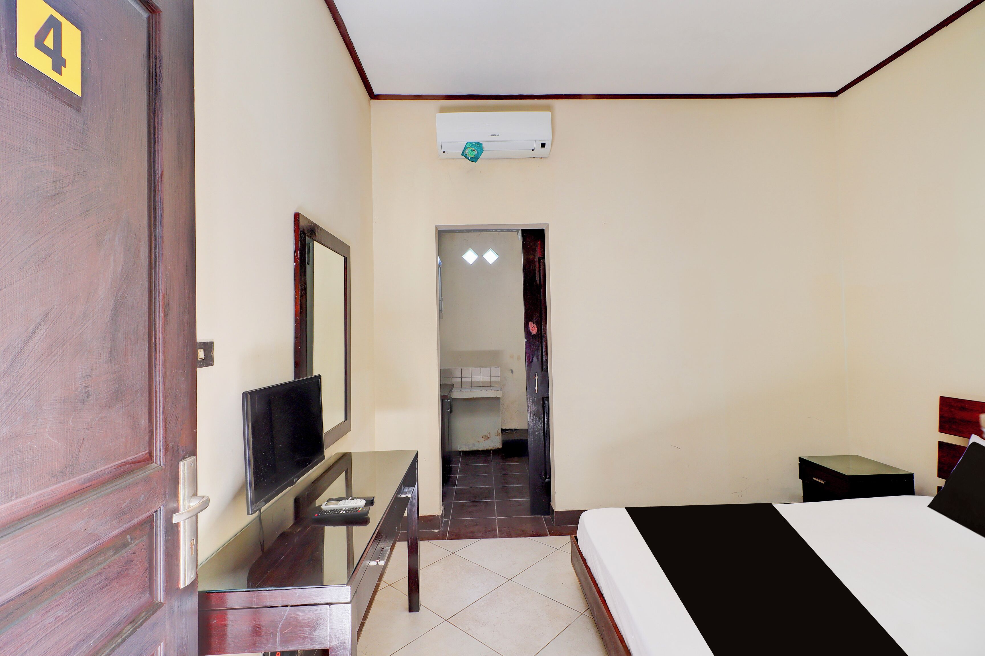 A hotel room with a bed, a desk with a TV, a wardrobe, and a bathroom visible through an open door.