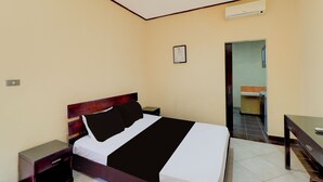 Quarto de hotel com cama, mesas de cabeceira, escrivaninha e aparelho de ar condicionado.
