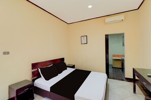 Una habitación de hotel con cama, mesitas de noche, un escritorio y un equipo de aire acondicionado.