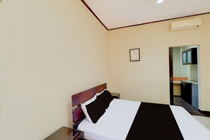 A hotel room with a bed, a nightstand, a framed picture on the wall, and a view of the kitchen through an open door. - Collection O Near Bali Royal Hospital Renon Formerly JC BoutiqueÂ Hotel (Denpasar)
