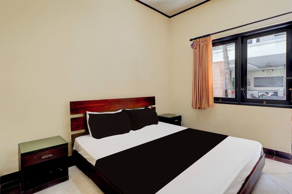 A bedroom with a bed, a nightstand, a drawer, and a window with curtains.