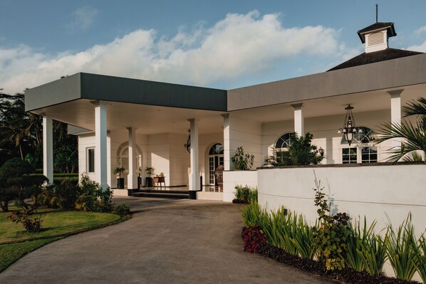 A modern building with a covered entrance, columns, and a garden. - CasCades Suites (Ubud)