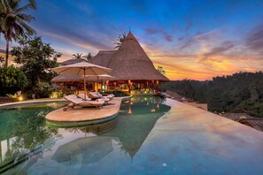 A resort with a pool, lounge chairs, and a thatched-roof building. - CasCades Suites (Ubud)