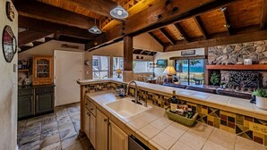 A kitchen with wooden beams, a stone fireplace, and a view of the outdoors.