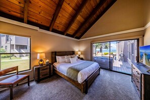 A bedroom with a large bed, a nightstand, a chair, a TV, and a balcony with a view of the ocean. - Lakefront 4BR Escape | Beach Access-Near Heavenly! (South Lake Tahoe)