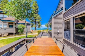 A wooden deck leading to a building with large windows, overlooking a beach. - Lakefront 4BR Escape | Beach Access-Near Heavenly! (South Lake Tahoe)