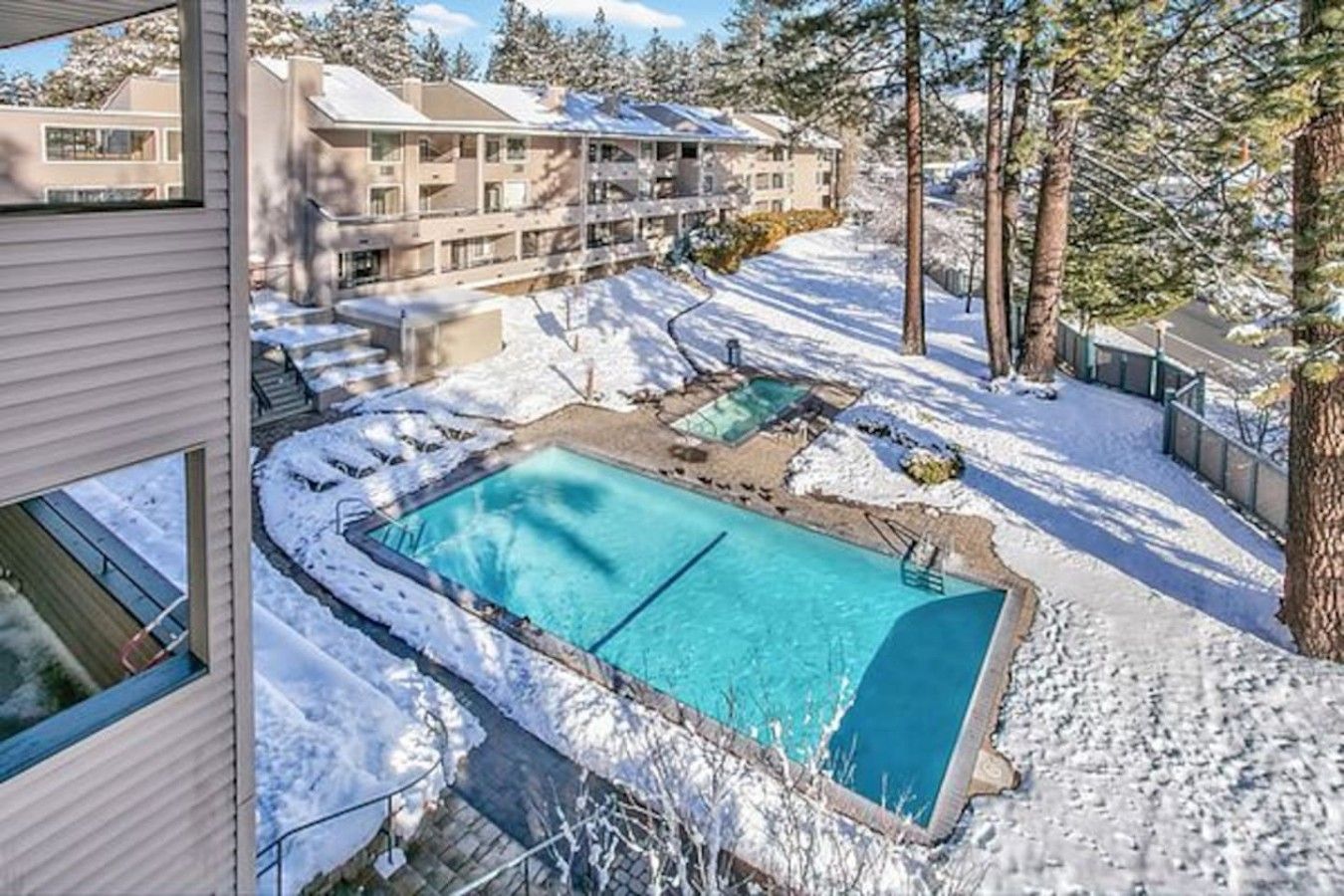 Une piscine entourée d’un paysage enneigé, avec un bâtiment visible au loin.