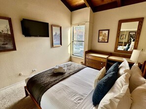 Un dormitorio con cama, cómoda, espejo y televisor en la pared.