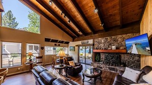 A spacious living room with leather sofas, a stone fireplace, and a television mounted above it.