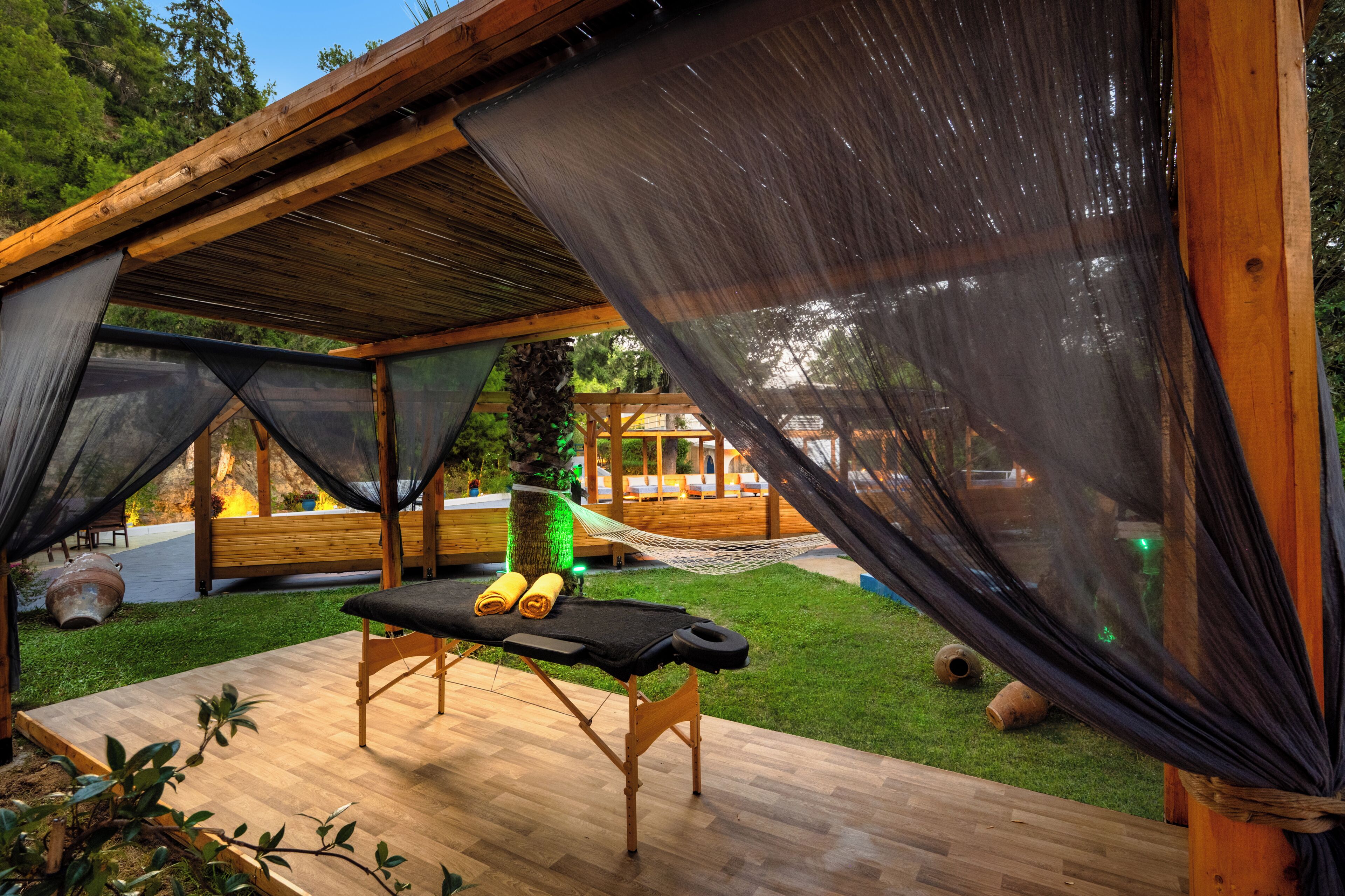 Uma área de relaxamento ao ar livre com uma rede, um banco e uma mesa de massagem.