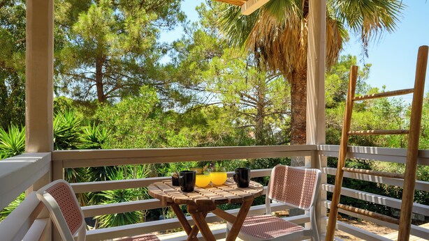 An outdoor seating area with a table and chairs, surrounded by a wooden railing, overlooking a lush garden with various trees and plants. - Trees Art Hotel & Suites (Rhodes)