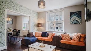 A modern living room with a sofa, coffee table, and a dining area. - Modern contemporary dog friendly - Licata's Apartment (Cirencester)