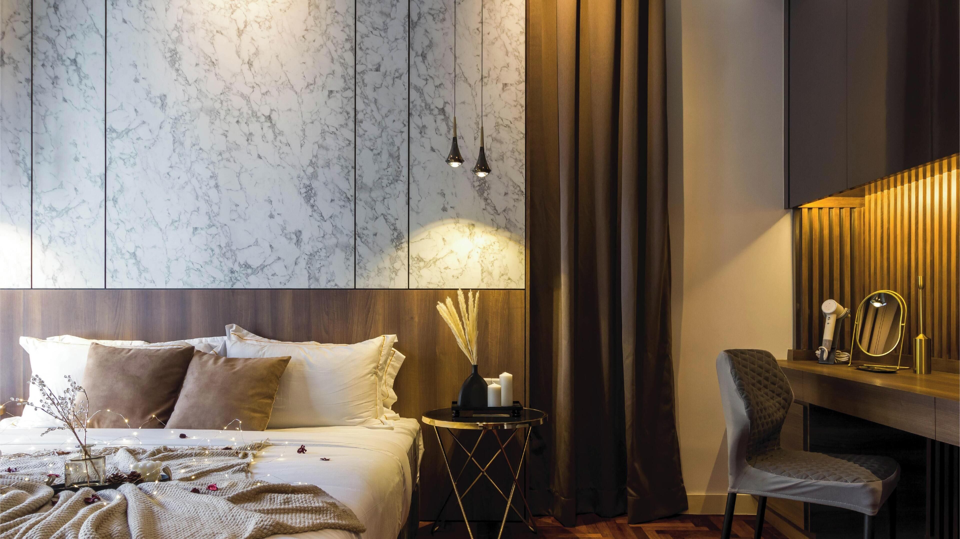 A modern bedroom with a marble-patterned wall, a bed with multiple pillows, a bedside table with a lamp, and a chair.