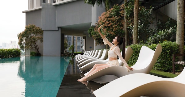 A poolside area with lounge chairs, a modern building, and greenery. - The Mews KLCC by Five Senses (Kuala Lumpur)