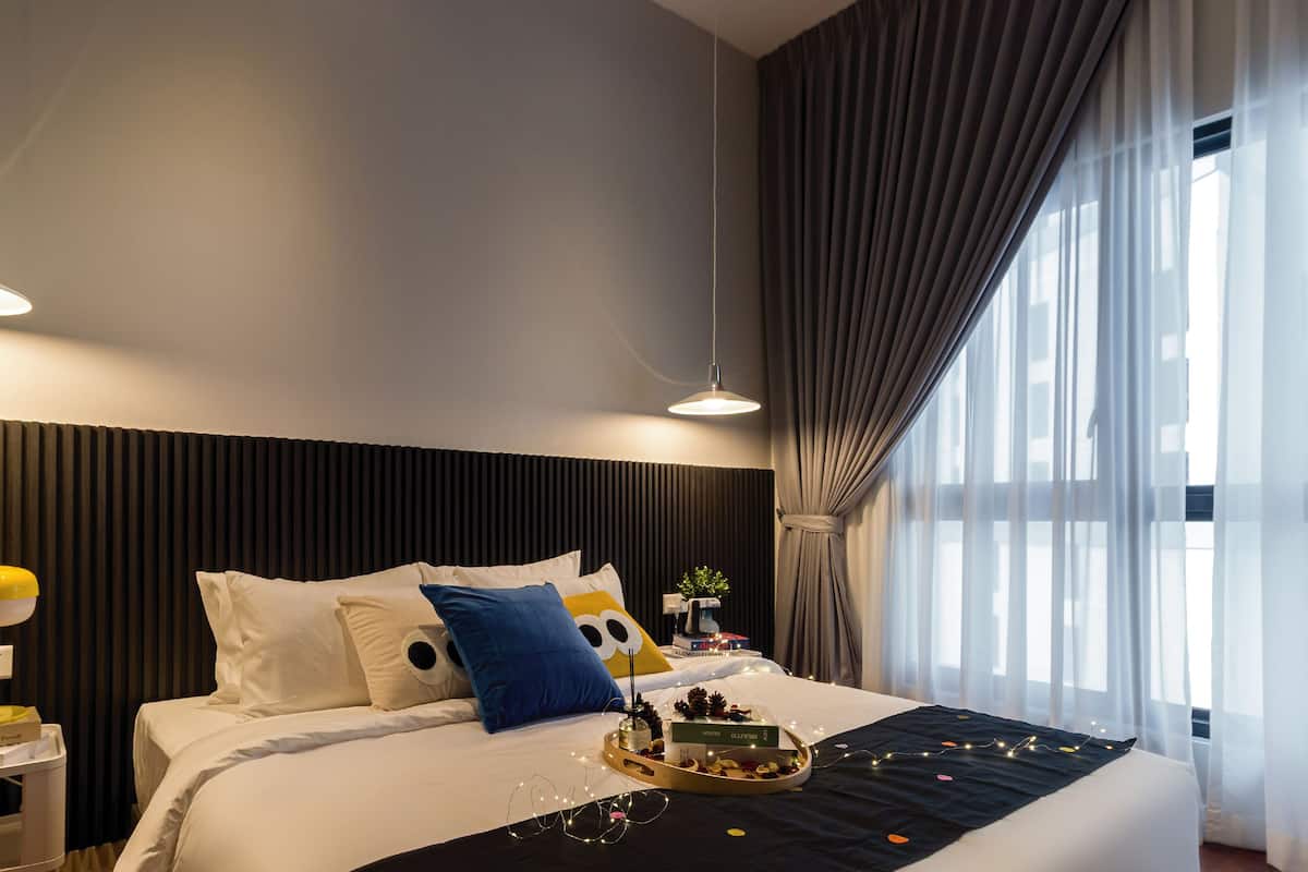 Una habitación de hotel moderna con una cama grande, dos mesitas de noche y un ventanal con cortinas.