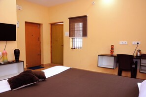 Une chambre d’hôtel équipée d’un lit, d’un bureau, d’une chaise, d’une télévision et d’une fenêtre avec des stores.