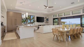 Una cocina moderna con una isla central, un comedor con mesa y sillas, un sofá blanco y un ventanal con vistas.