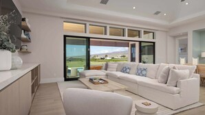 Un salón moderno con un sofá blanco, una mesa de centro y vistas a un paisaje verde a través de amplios ventanales.