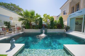 A swimming pool with a water fountain, surrounded by lush greenery and modern outdoor furniture. - Luxury Short Term Stay 2BHK plus Maids - RANCHES (Dubai)
