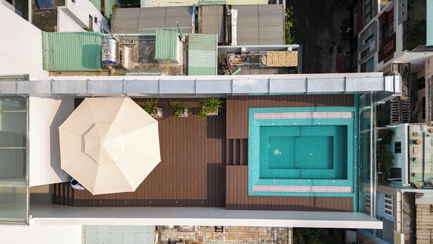 Une piscine sur le toit, avec une terrasse en bois, un grand parasol et des plantes en pot.