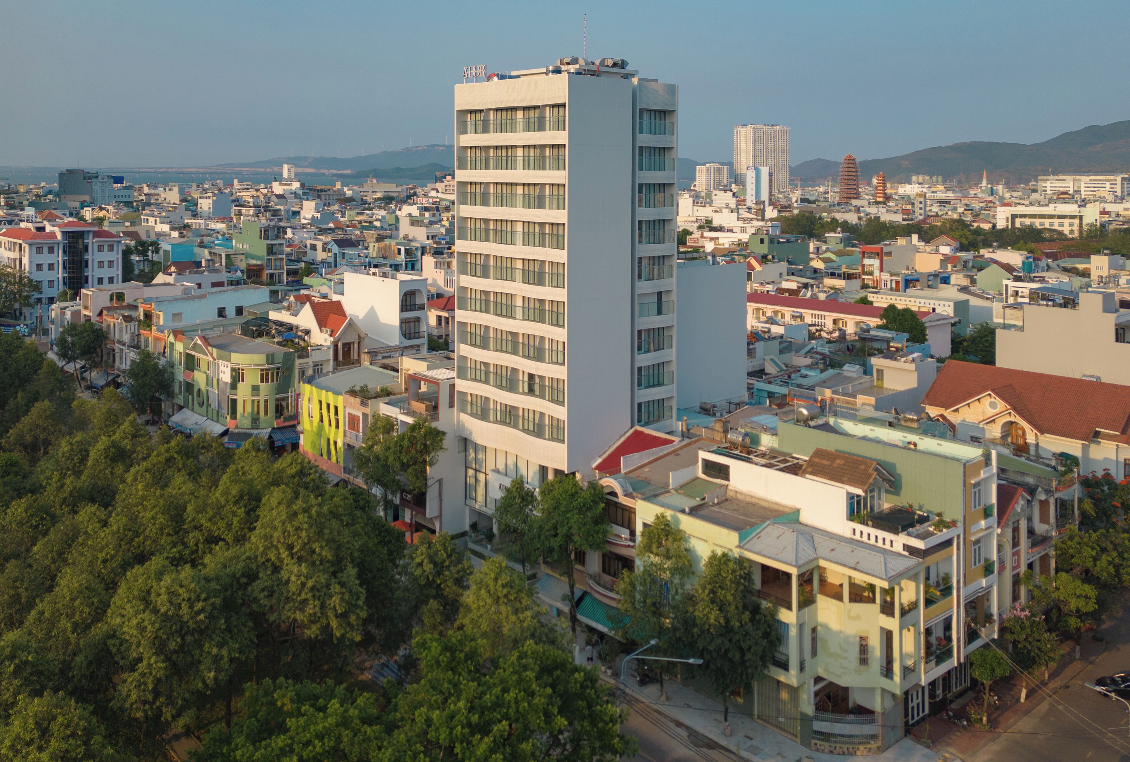 Un edificio de gran altura con varios pisos, rodeado por una zona urbana densa con diversos edificios y zonas verdes.