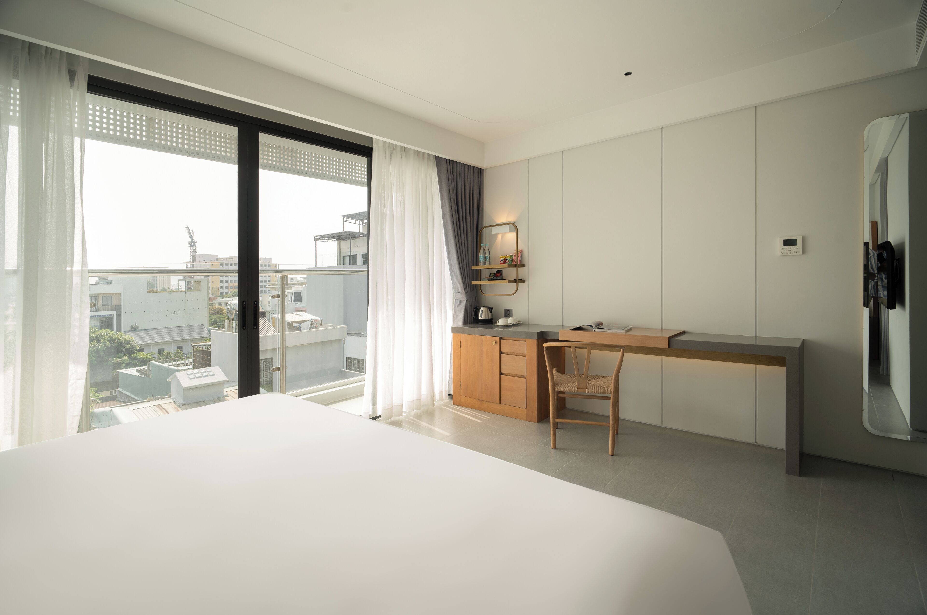 A modern hotel room with a large bed, a desk, and a view of the city.