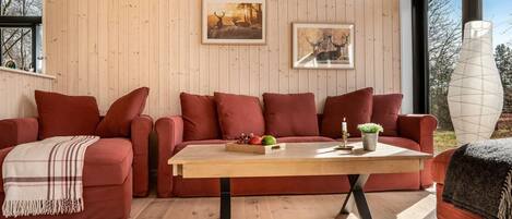 Un accogliente soggiorno con soffitto in legno, un divano rosso, un tavolino da caffè in legno e quadri appesi alle pareti.