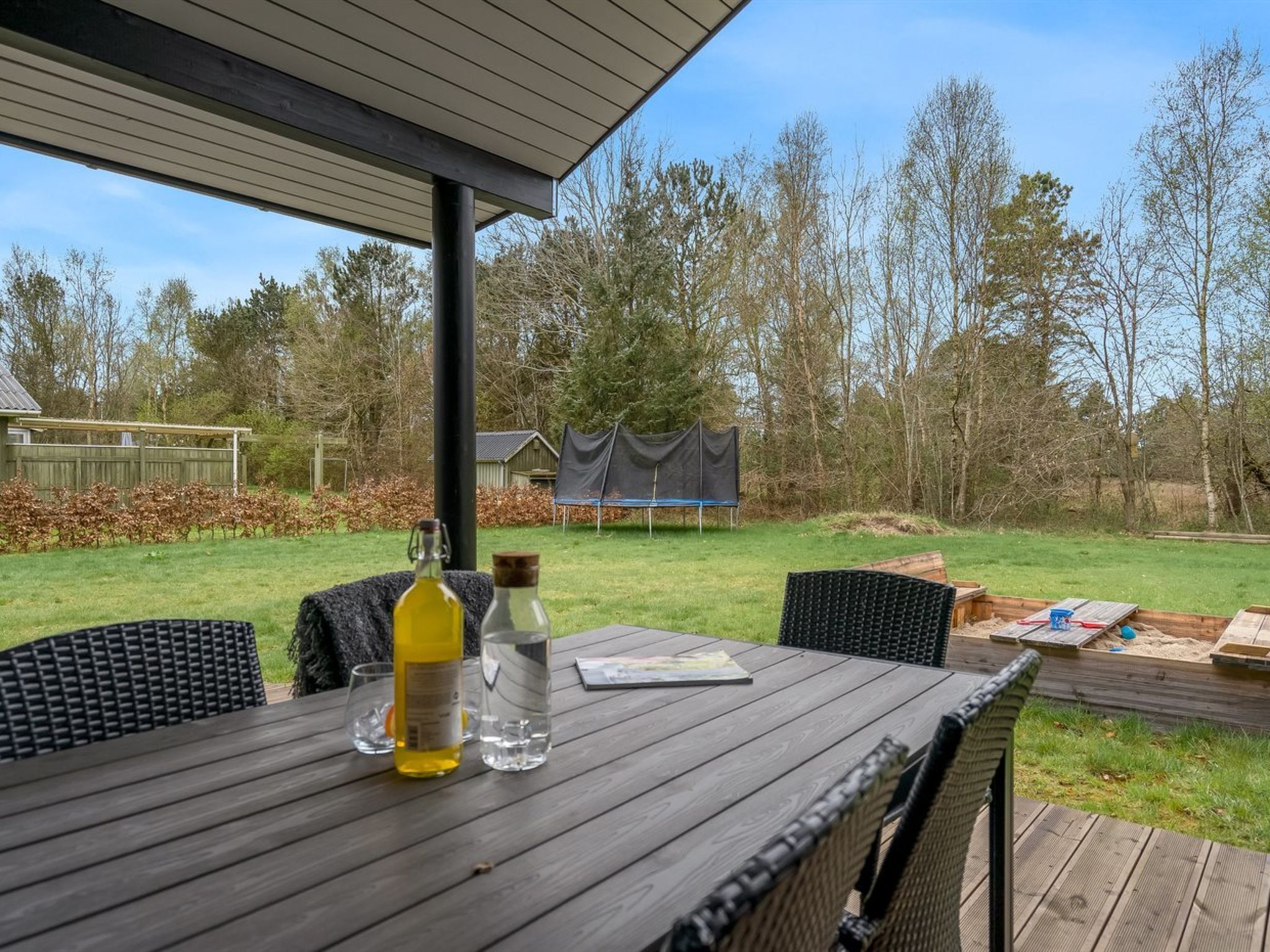 A covered outdoor area with a table, chairs, and a view of a grassy yard and trees.