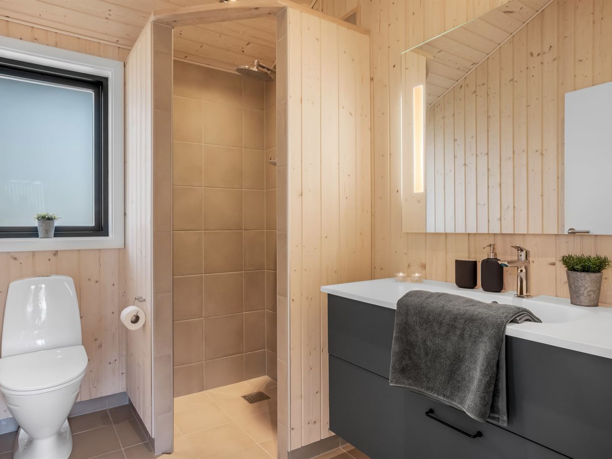 Ein modernes Badezimmer mit Holzvertäfelung, einer weißen Toilette, einer Dusche und einem Waschtisch mit einem Handtuch.