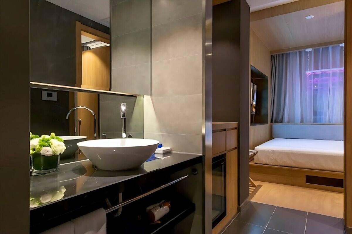 A modern bathroom with a large mirror, a white sink, and a small flower arrangement.