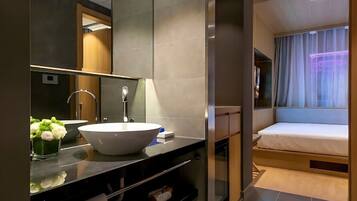 A modern bathroom with a large mirror, a white sink, and a small flower arrangement.
