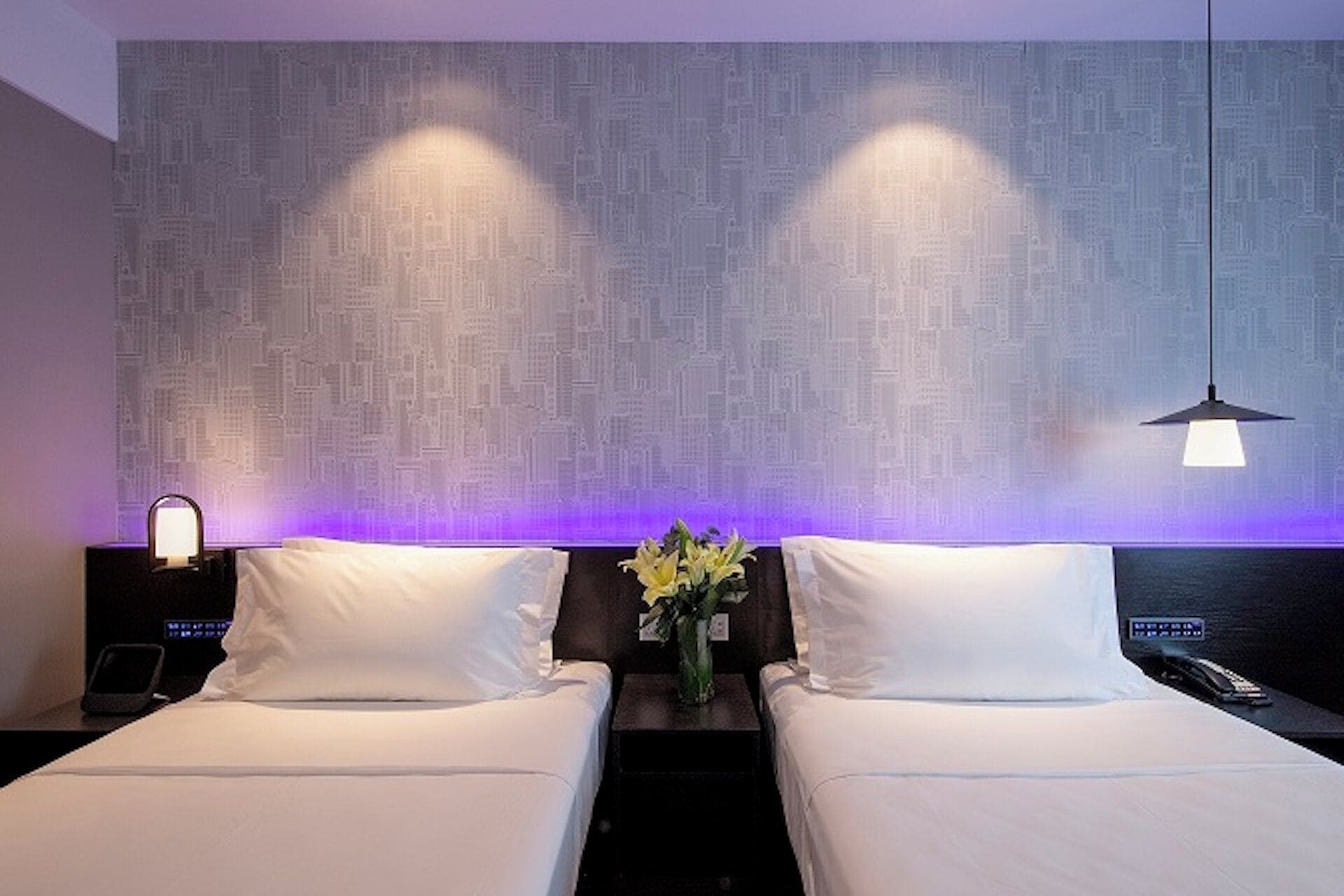 Ein Hotelzimmer mit zwei Betten, einem Nachttisch mit Lampe und einer Wand mit einem Schaltkreis-Muster.