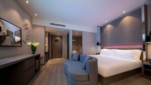 Une chambre d’hôtel moderne dotée d’un grand lit, d’un espace salon aux lignes arrondies, d’un bureau et d’un miroir.